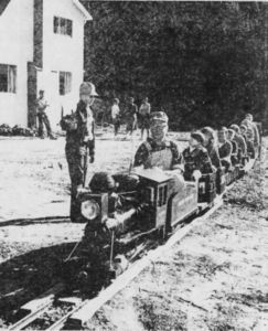 The Raccoon Gulch Express pulls out of its "depot" with a load of youngsters from the Cascade neighborhood of Fairfax. Owner of the small railroad is Gordon B. Adams, shown piloting his electric "steam engine." Flagging the crossing is Sellar Nugent, 13, of Ross. The railroad is located on Adams' two acre property of 475 Cascade Drive. From Independent-Journal, Saturday, March 18, 1961