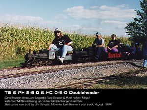 Carol Harper drives Jim Leggett's Toad Swamp & Punk Hollow 'Mogul' with Fred Motten following up on his Hullo Central yard switcher. Both locos were built by Jim Turnbull. Montreal Live Steamers club track, August 1994. From TrainNet.org.